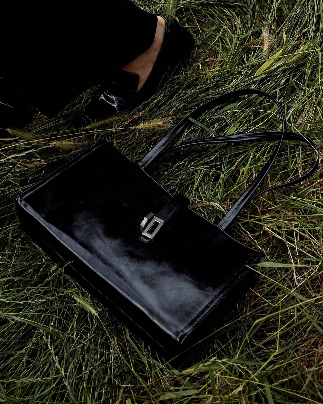 Black MJade bag with silver hardware placed on grass.