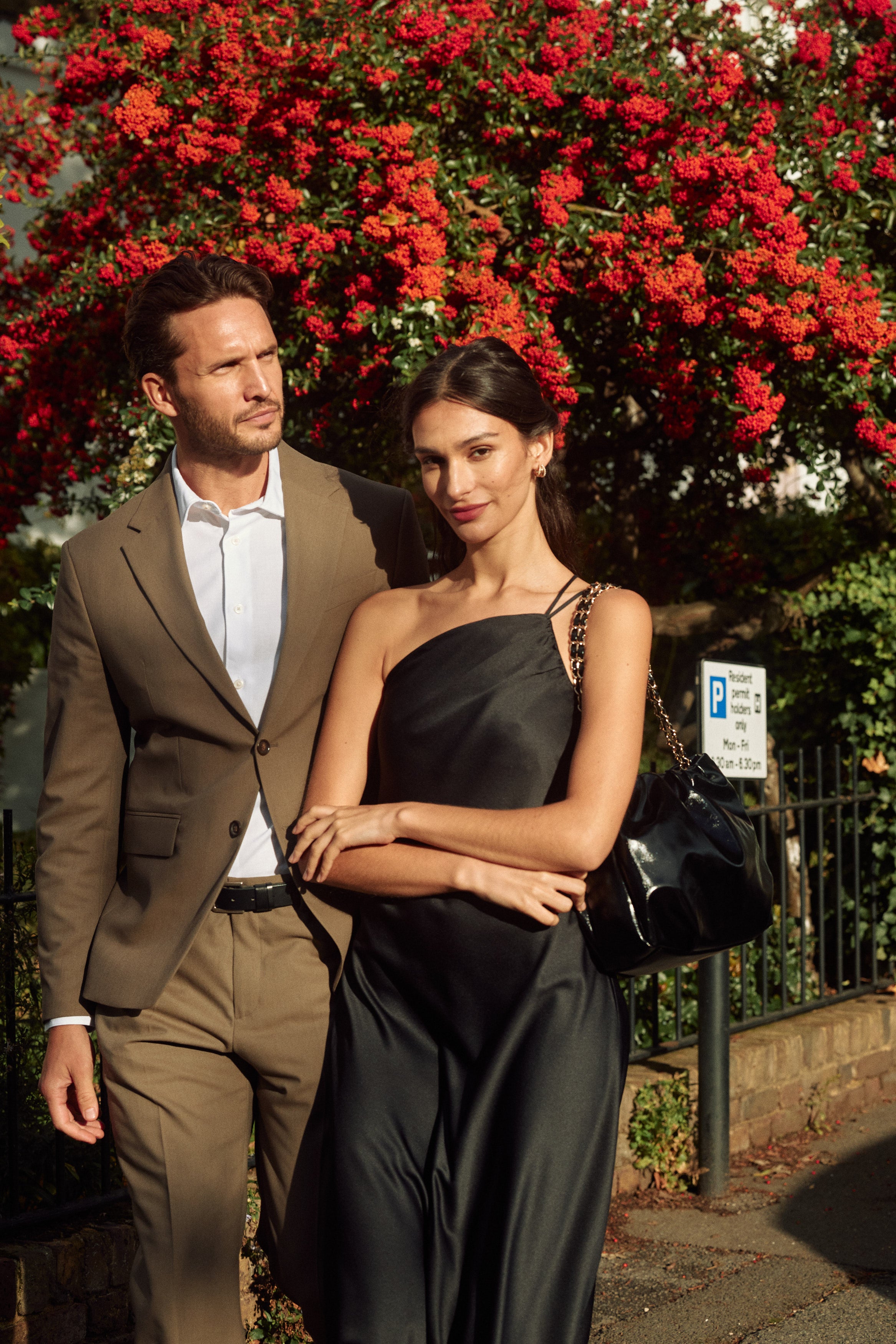 A couple standing beside flowering greenery in a London neighbourhood.