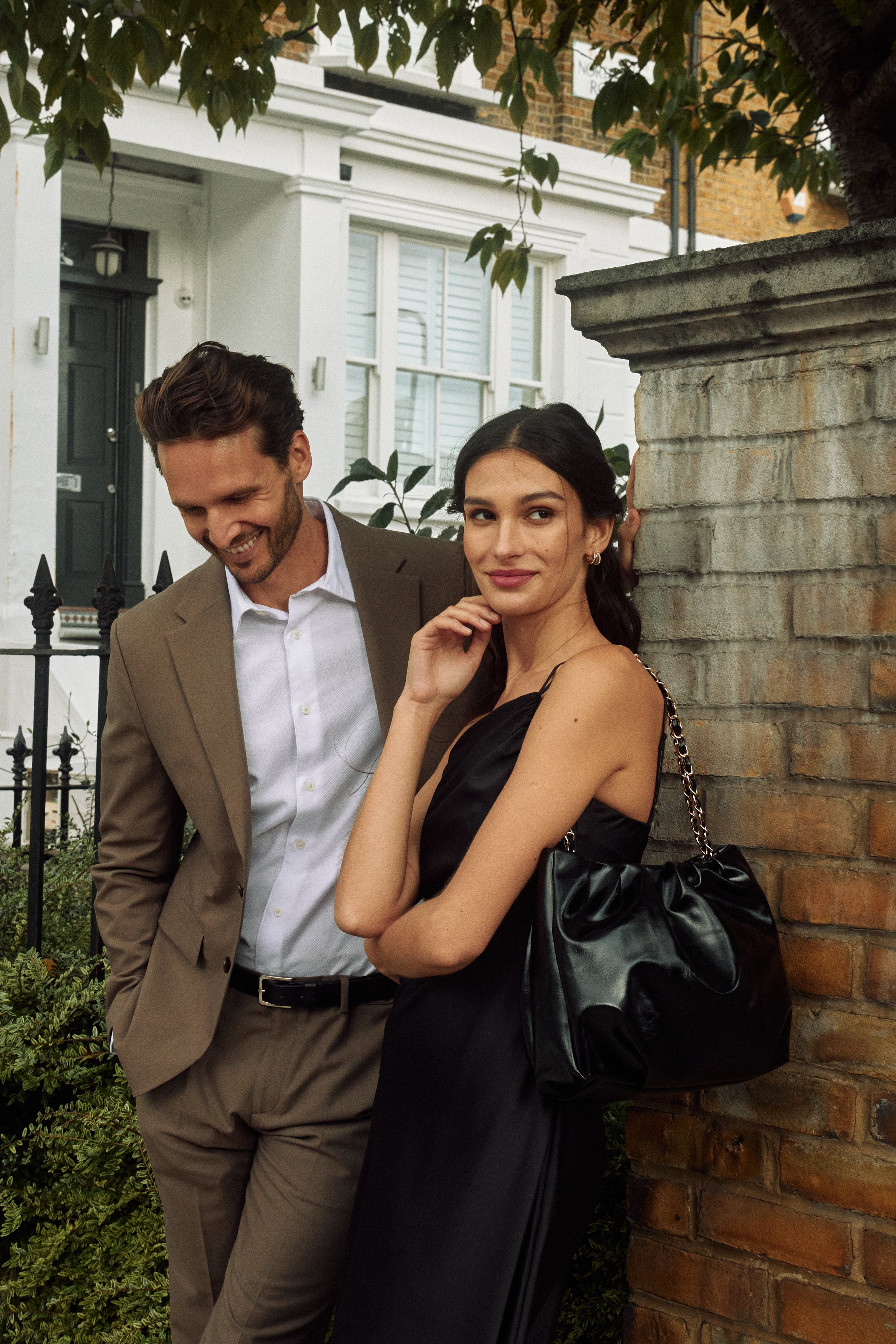 A couple standing together beside a brick wall in a residential London street.