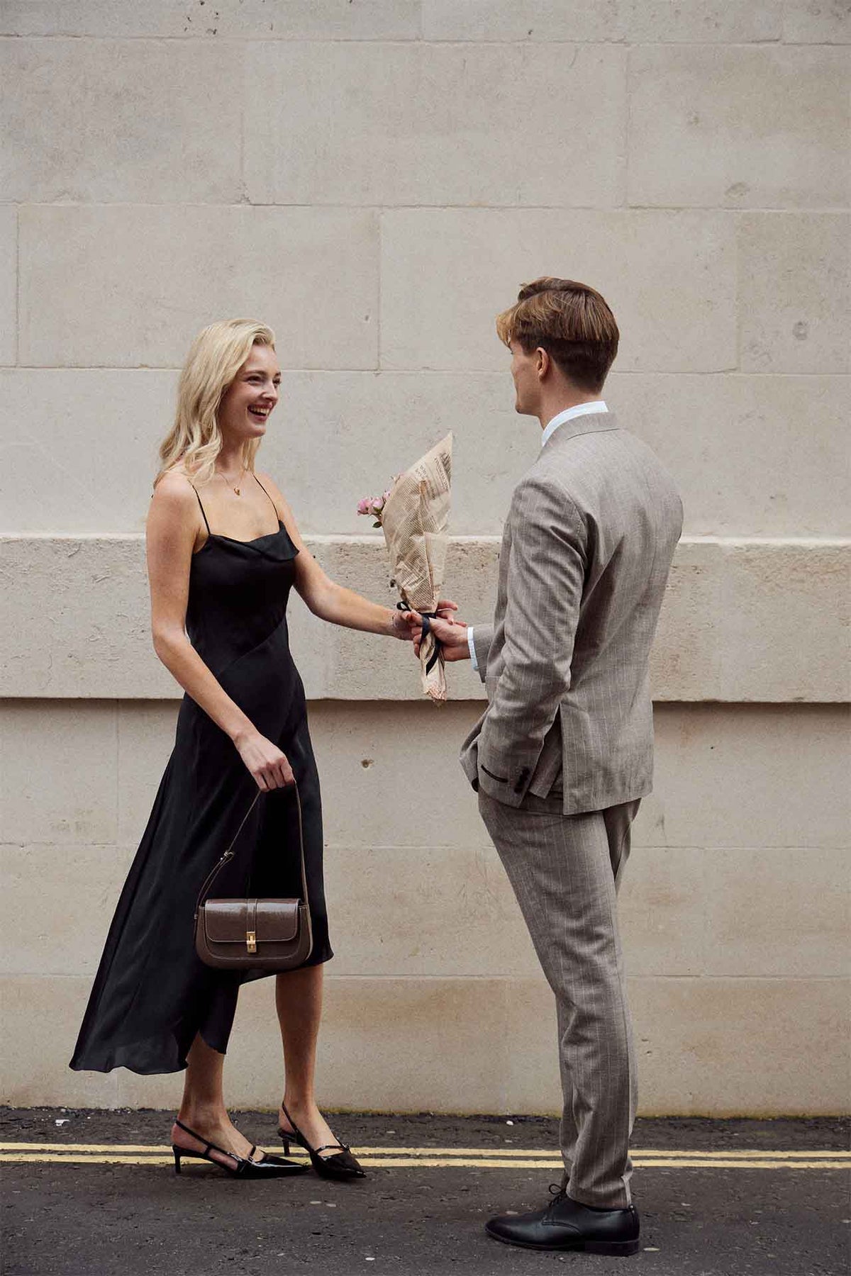 A man holding flowers behind his back as a woman approaches.