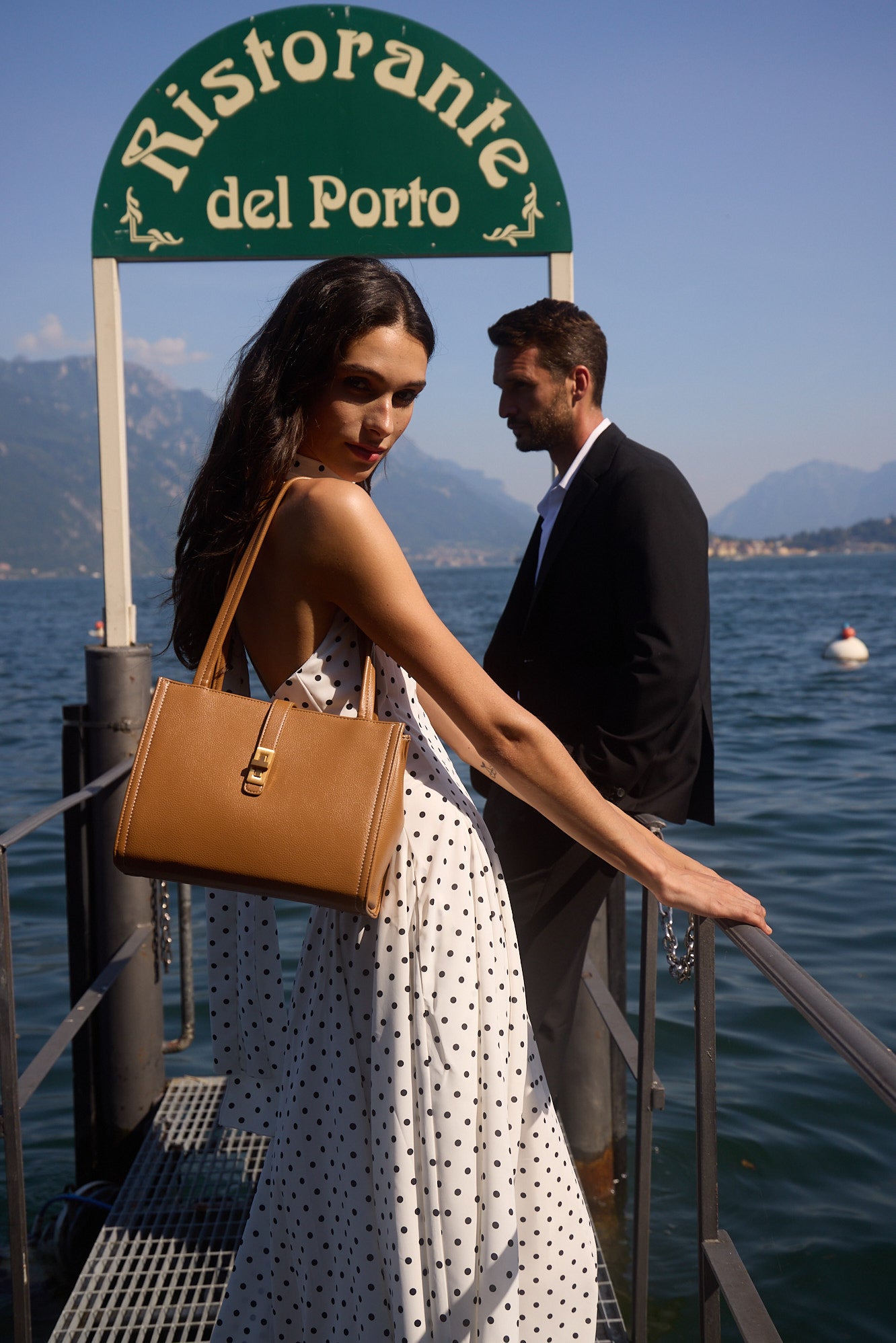 A woman carrying a tan MJade handbag on a waterfront landing at Lake Como.