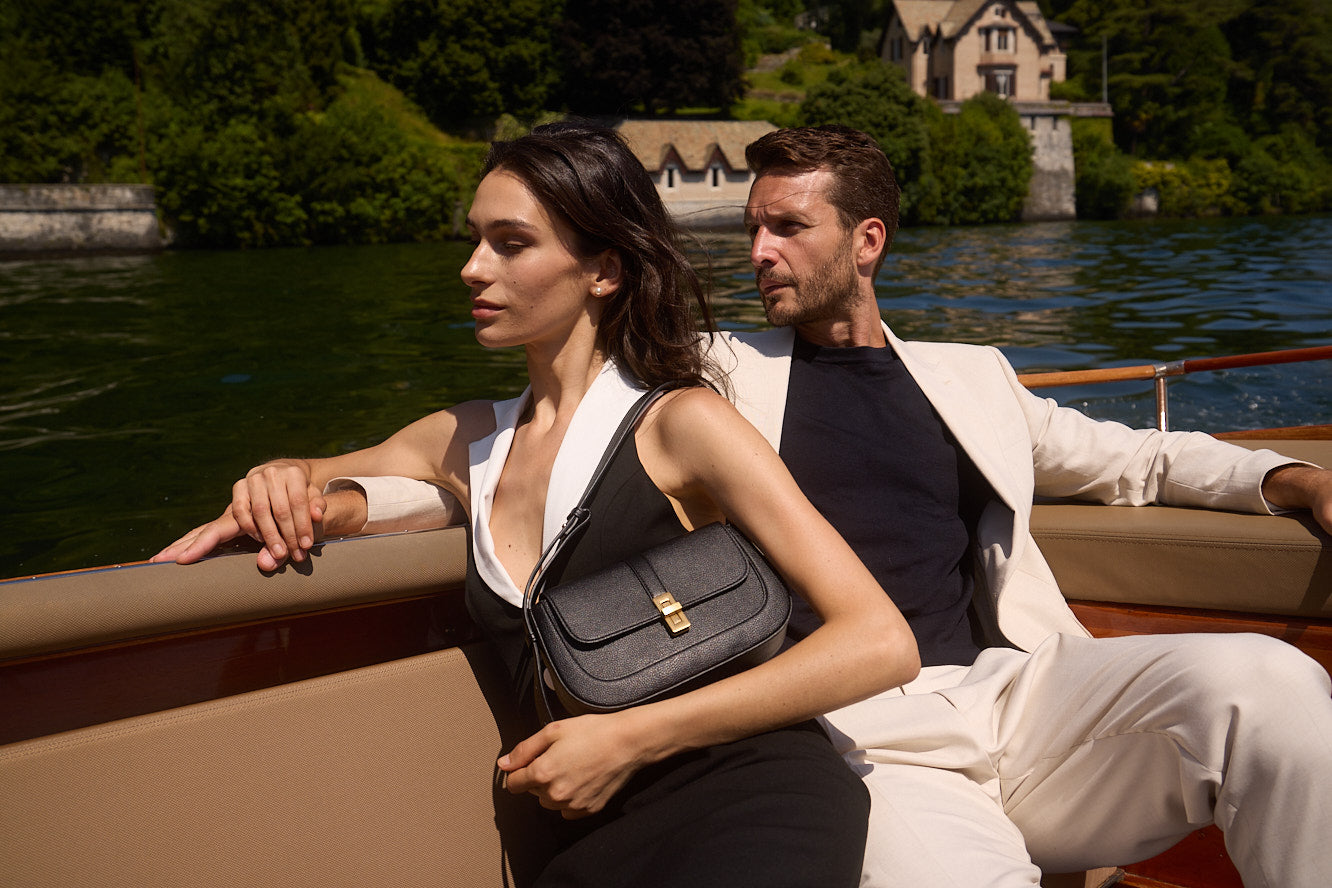 A couple seated together on a boat on Lake Como with a black MJade handbag.